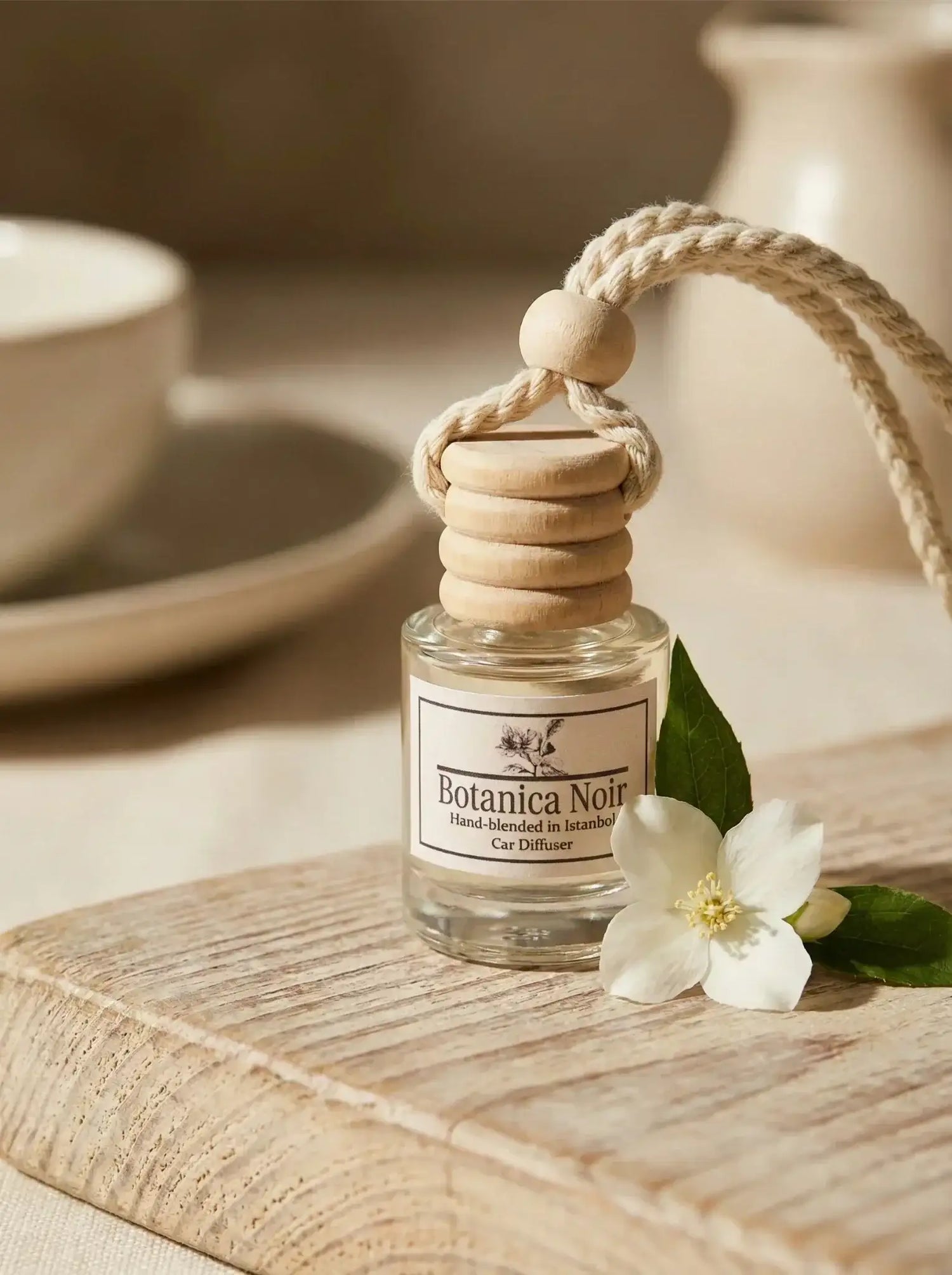 Ahşap kapaklı cam şişede oda kokusu ve yanında beyaz çiçek, doğal dekor