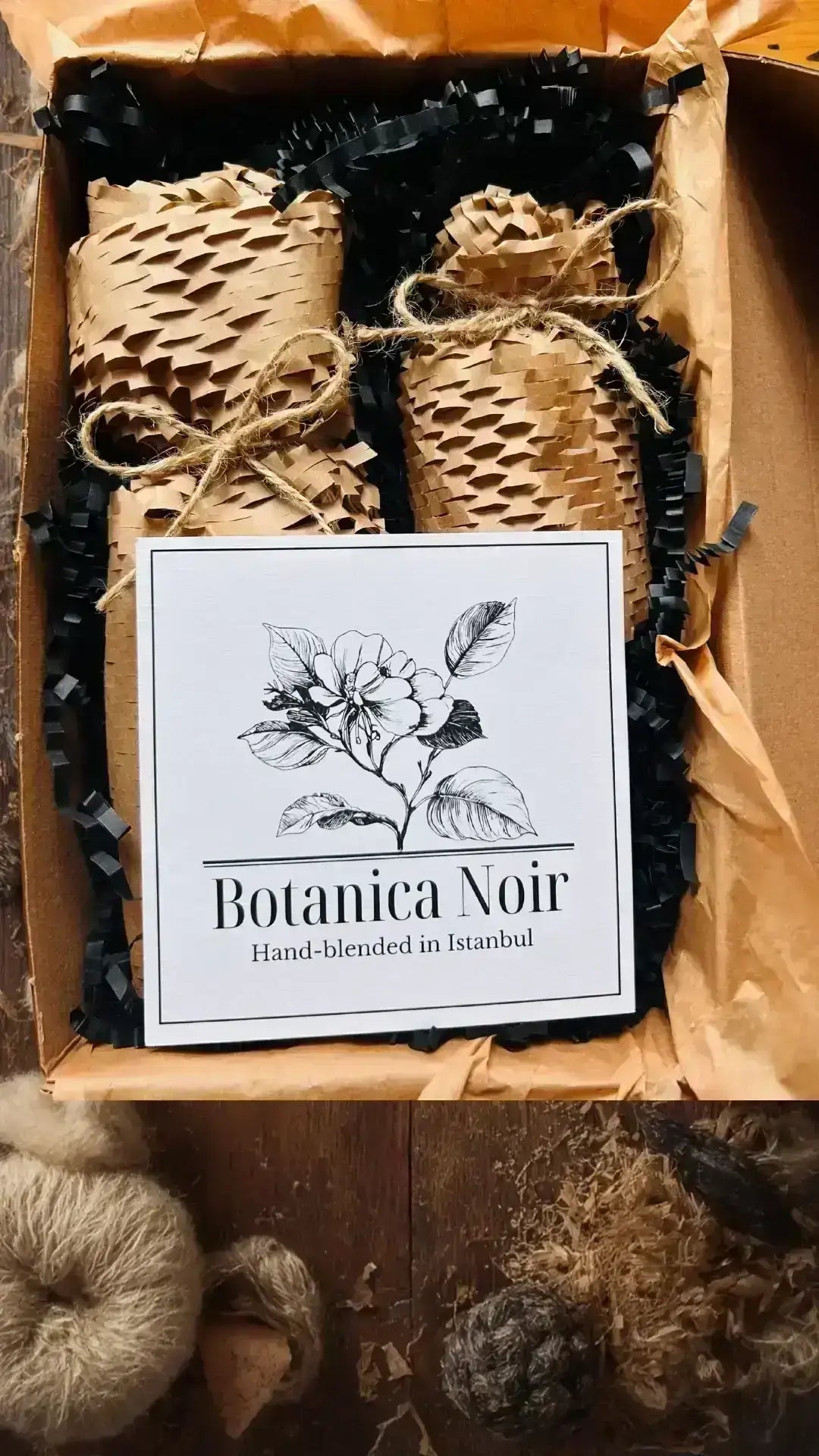 Kraft kağıda sarılı ve ip ile bağlanmış oda kokusu seti, siyah dolgu malzemesiyle kutuda sunuluyor.